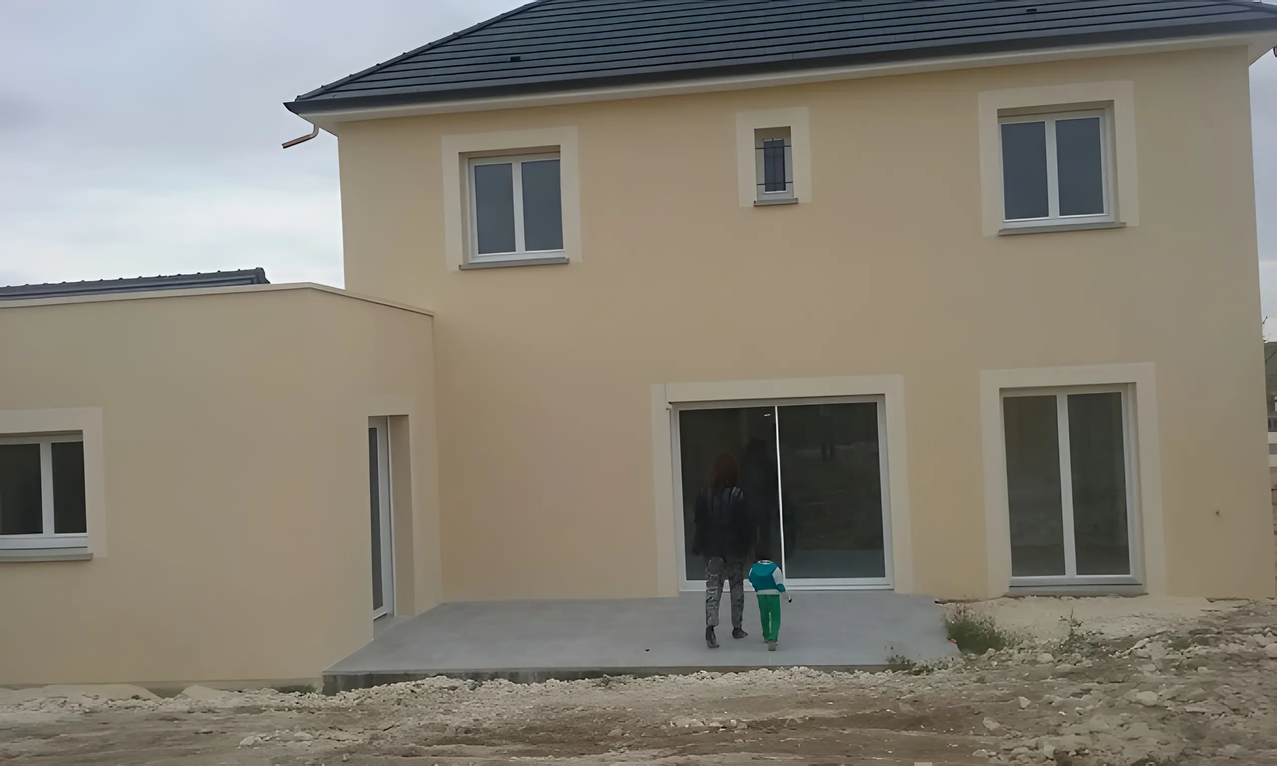 Maison à étage à façade beige, fenêtres blanches et baie vitrée au rez-de-chaussée